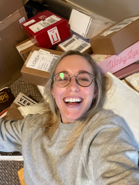 A woman laughing wearing glasses laying on top of a pile of packages